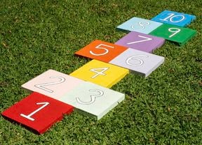 Bright painted paver tiles with numbers are arranged on grass to form a reusable hopscotch path for kids to play outdoors.