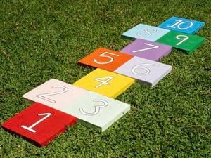 Bright painted paver tiles with numbers are arranged on grass to form a reusable hopscotch path for kids to play outdoors.