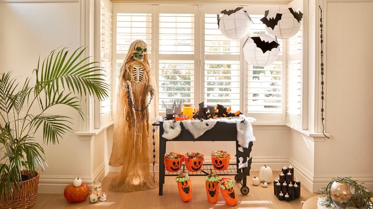 A tabletop with black cups, striped straws, a jug of orange drink, a bowl of punch, and scattered Halloween-themed decorations like spiders and cobwebs.