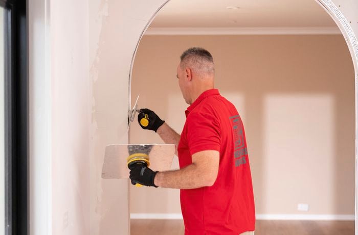 A Bunnings Team Member is applying plaster across the surface of the arch using a trowel and a hawk.