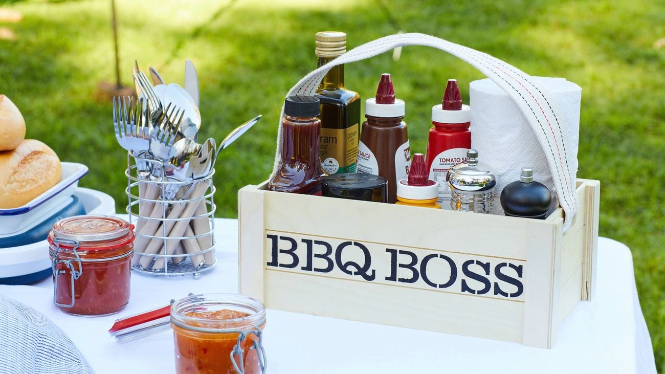 A sauce carrier labelled BBQ Boss on a table with cutlery, sauces and breadrolls.