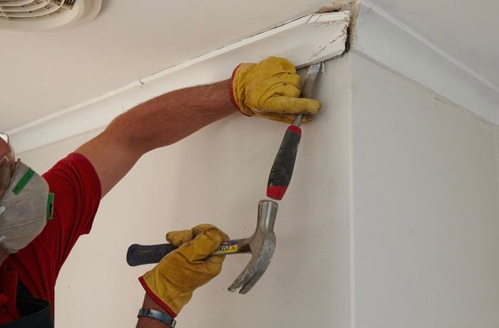 A person removing cornice with a hammer and chisel