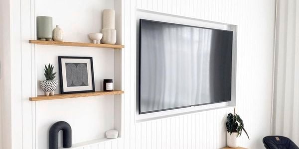 Living room with white painted timber panelled wall with an inset mounted TV next to timber shelving and a storage bench