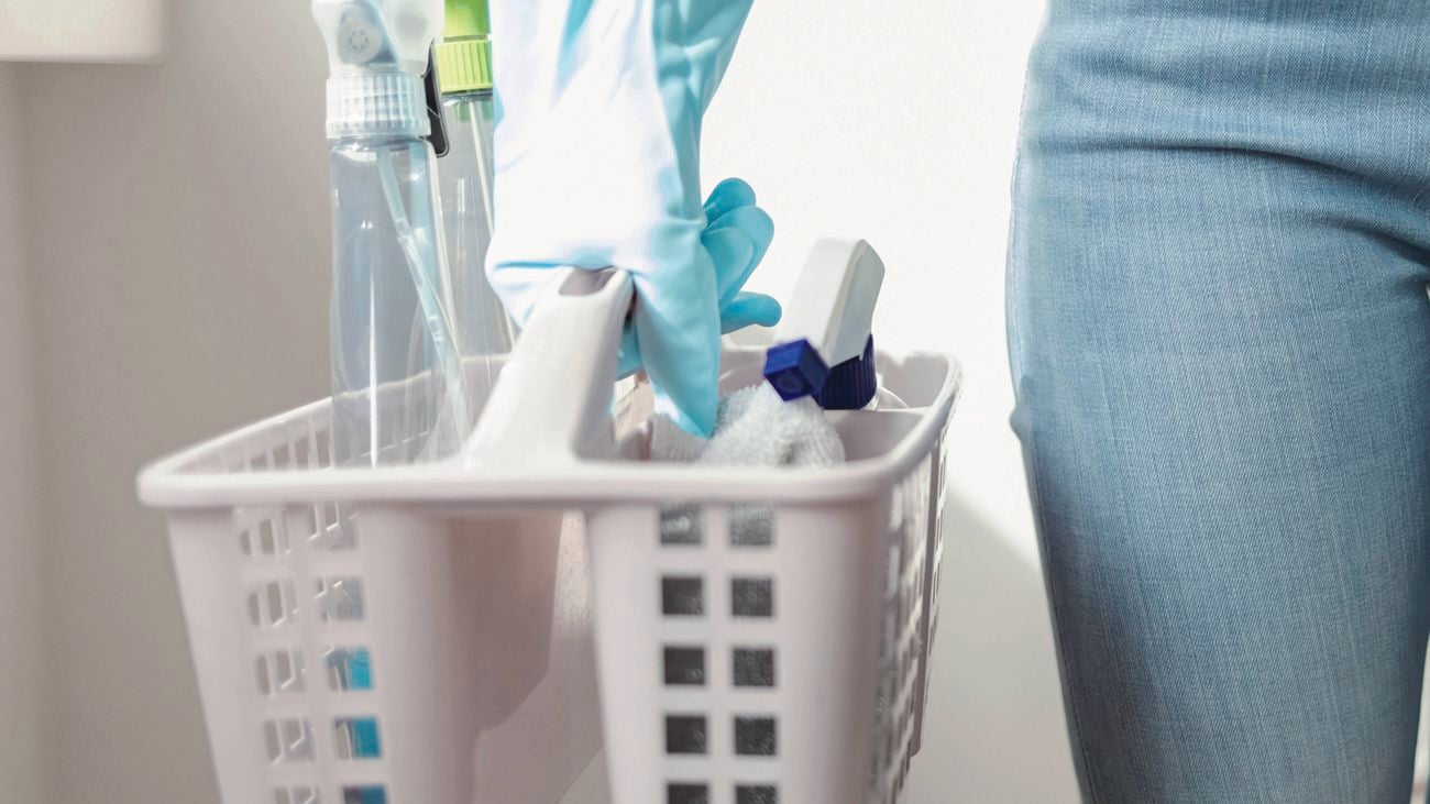  A hand wearing a blue rubber glove holds a white plastic cleaning caddy filled with cleaning products