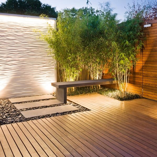 Timber decking and decorative ripple standing feature with surrounding pebbles, pavers and small trees.