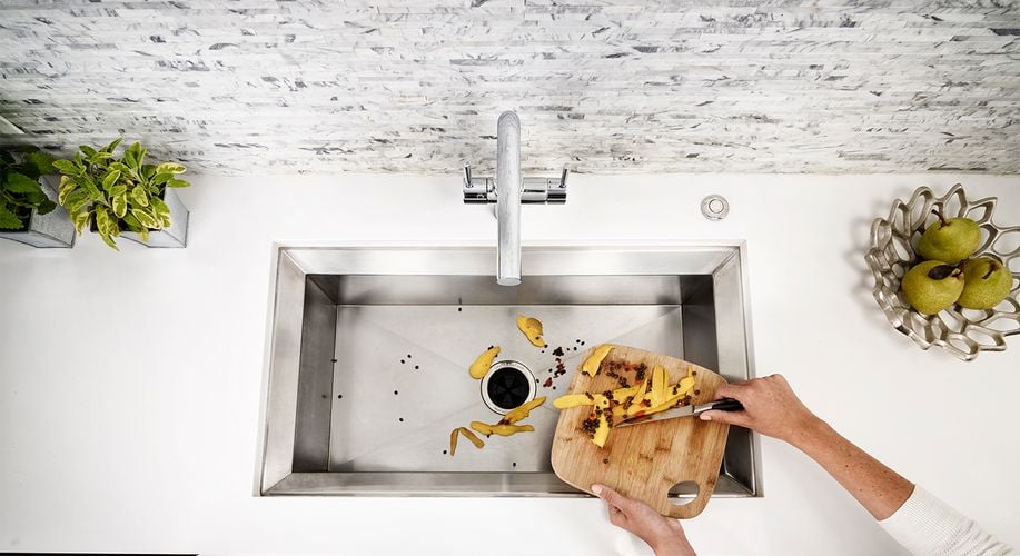 Person scraping food scraps off a chopping board into sink