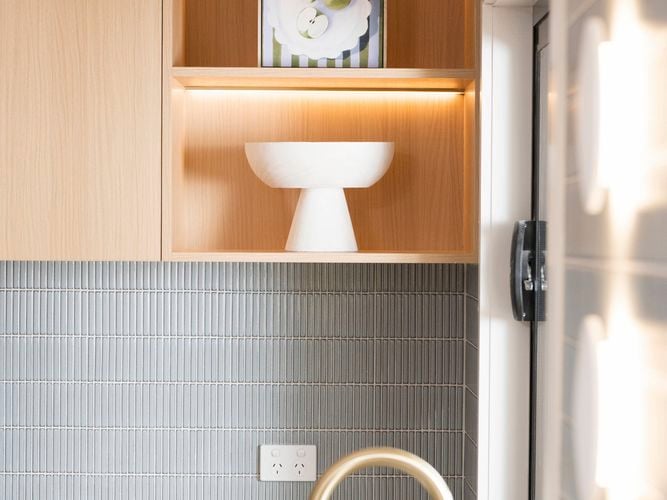 A kitchen with brown shelving with a vase and a picture frame on it, grey splashback and a white benchtop in it.