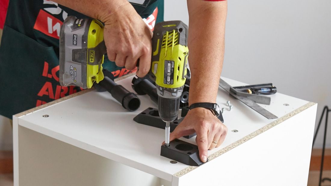 Person drilling plastic feet to bottom of linen chute cupboard.