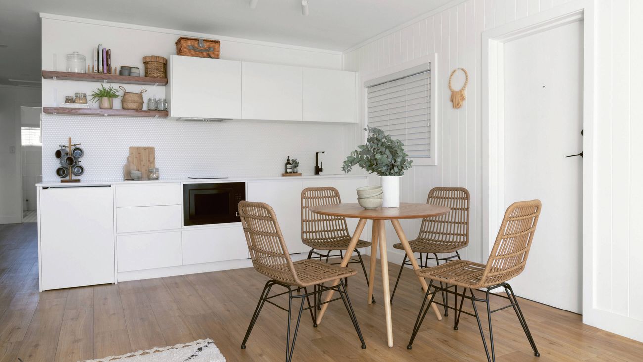 A modern kitchen and dining area with white cabinetry, a wooden dining table, and four woven chairs.