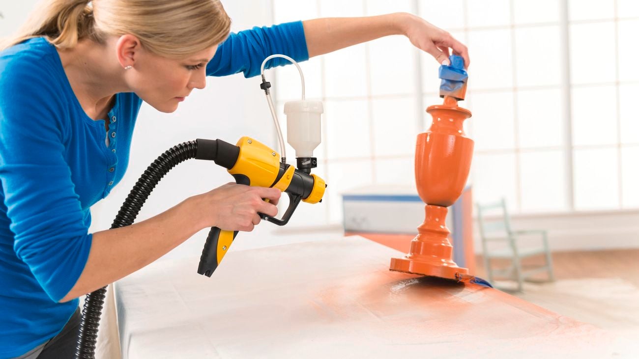 lady using a spray gun to paint a lamp base in orange paint