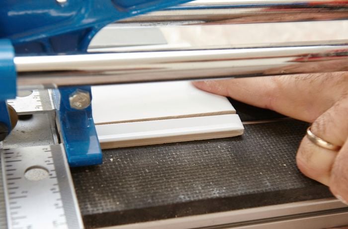 Person using tile cutter to cut a tile.