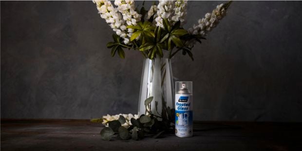 Frosted glass can on table with flower vase in background.