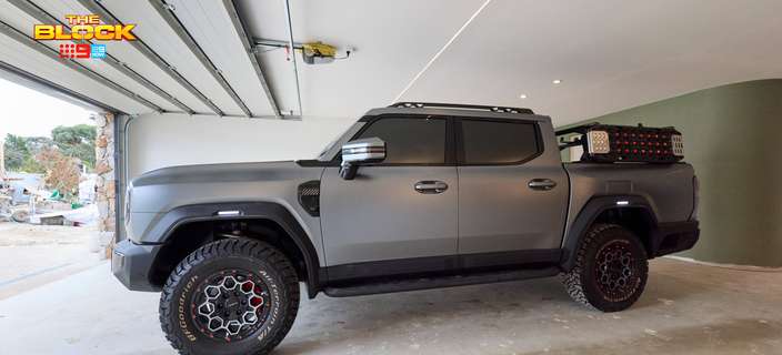 Modern garage featuring a grey four-wheel-drive ute with off-road tyres, concrete flooring and an open roller door.