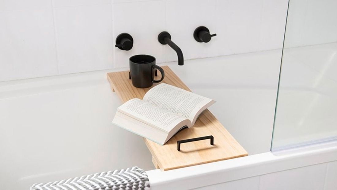 A wooden bench with book and mug resting across a bathtub