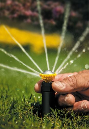 Close up of person adjusting a sprinkler head with water spraying out