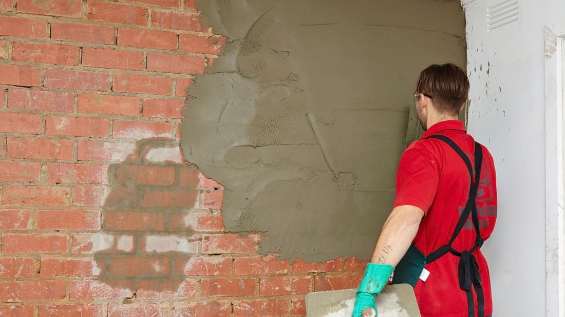 A person applying cement plaster to a brick wall using a trowel