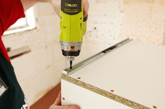 Drawer runners being drilled into the bottom of a cabinet drawer