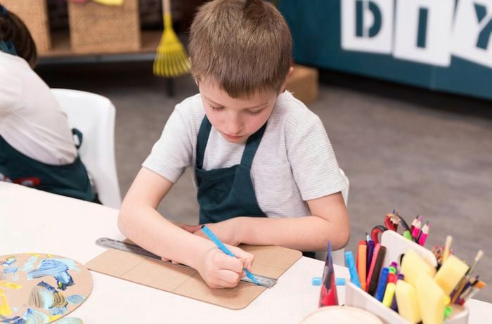 A boy is drawing vertical and horizontal blue lines with a ruler.
