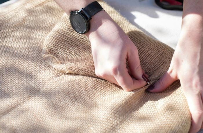 Person safety-pinning hessian together.