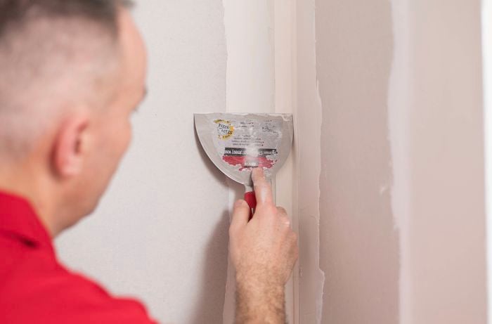 A person in a red T-shirt is applying a thin coat of base compound to the internal corners