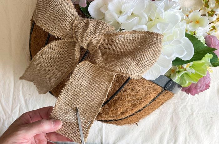 Close-up of a hand cutting burlap with scissors on a coir-lined hanging basket