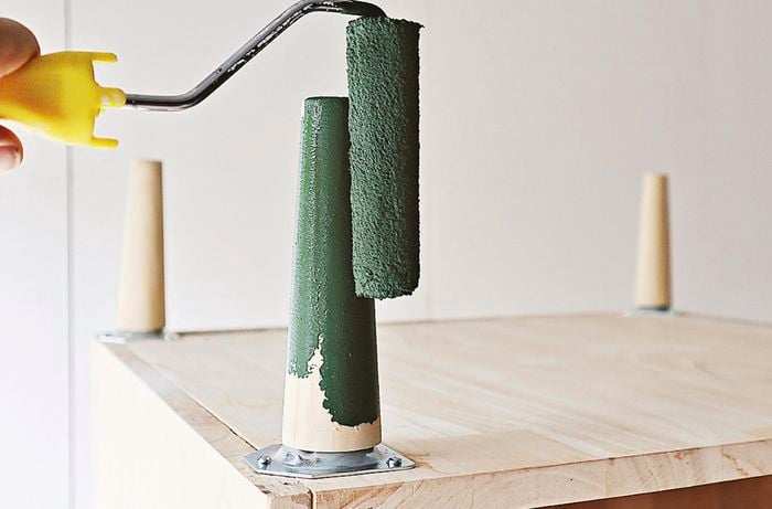 Close up of a person using a paint roller to paint bedside table legs green