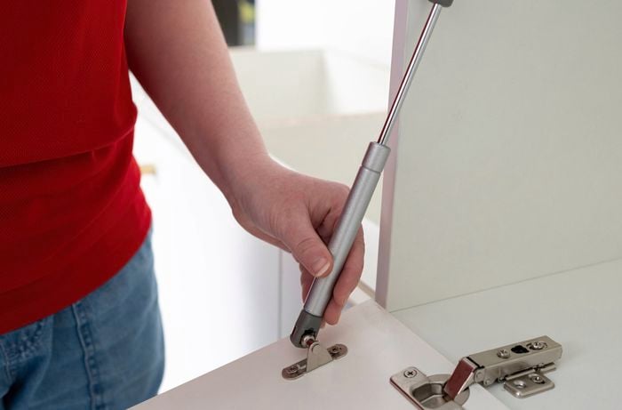 A person is adjusting a door bracket on the gas strut to the inside of a cabinet.  
