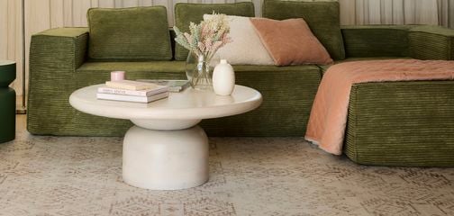 Living room while soft white sheer curtains, green and cream lounge with soft colour cream rug. 