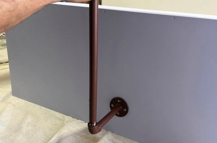 A close up of a hand holding brown-painted pipework and flange in place against the bench seat