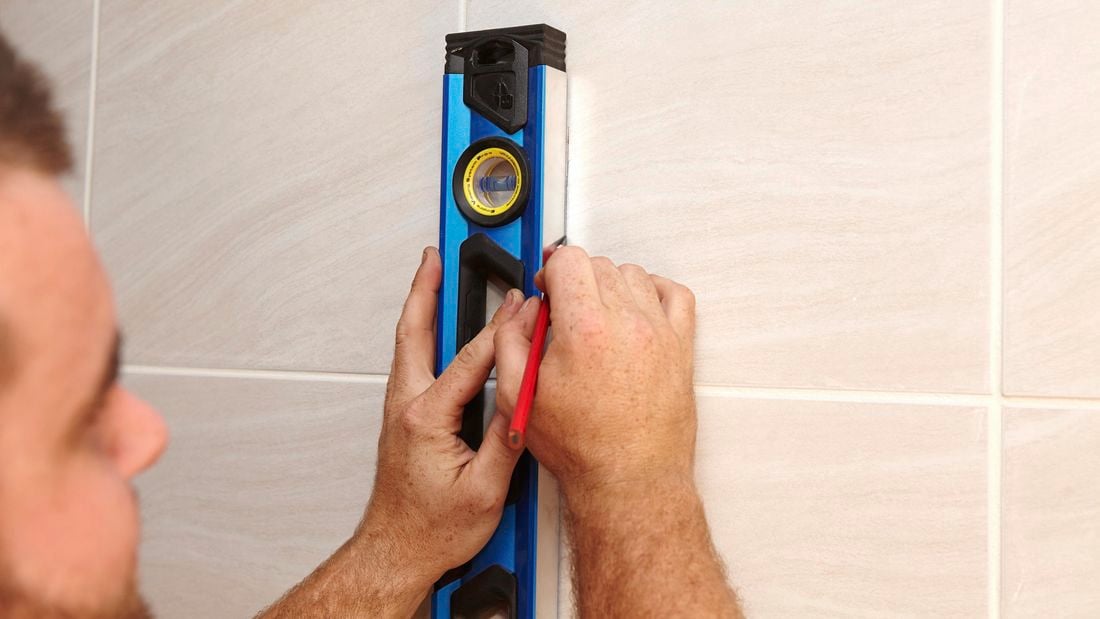 A person marking a tile wall using a set square