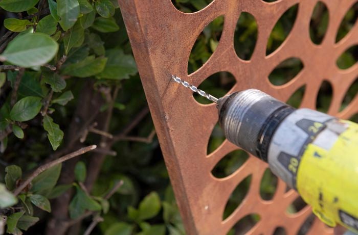 A person drilling a hole in a steel screen panel