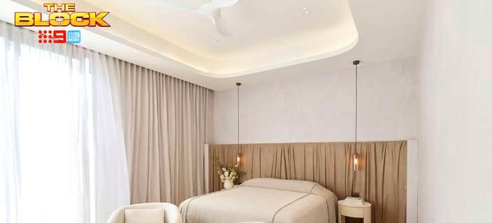 Serene neutral-toned bedroom with a timber feature headboard, upholstered bed, pendant lights, curved armchairs and floor-to-ceiling curtains.
