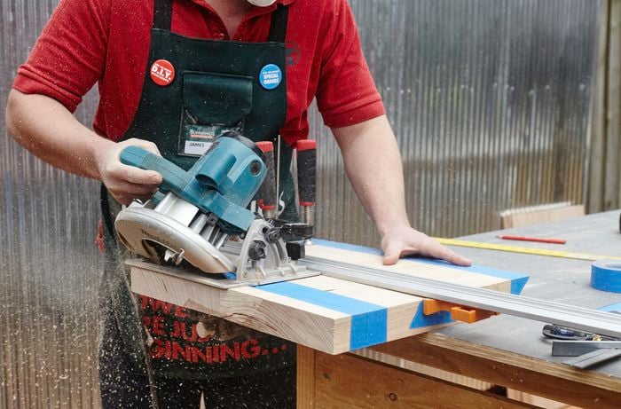A person sawing a piece of timber on a 45 degree angle using a circular saw