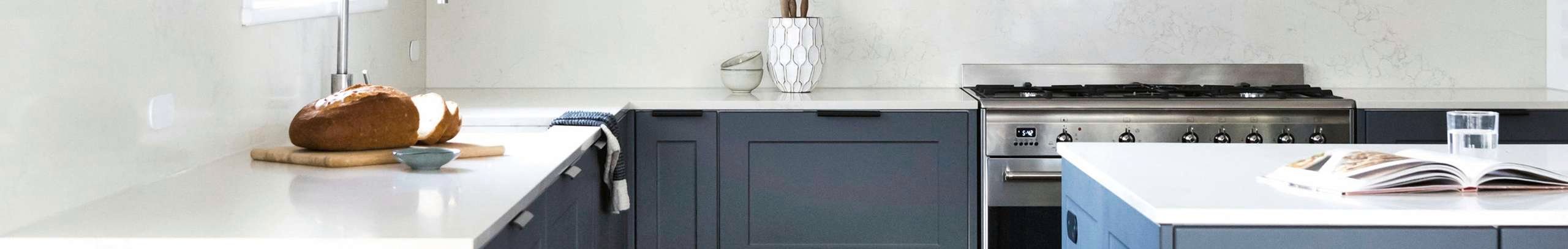 Blue cabinets with white benchtop kitchen stocked with silver taps and floating shelving 