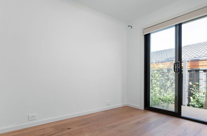 An image depicts a room featuring white walls and ceiling, with brownish flooring and a slider.