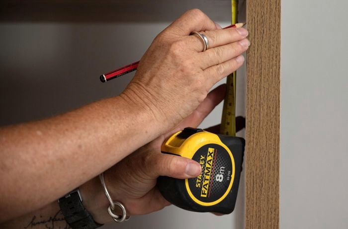 A person holding a measuring tape and a pencil