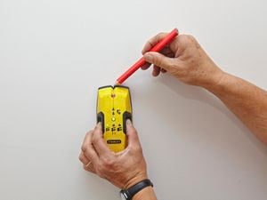 Using a stud finder to find and mark the wall studs.