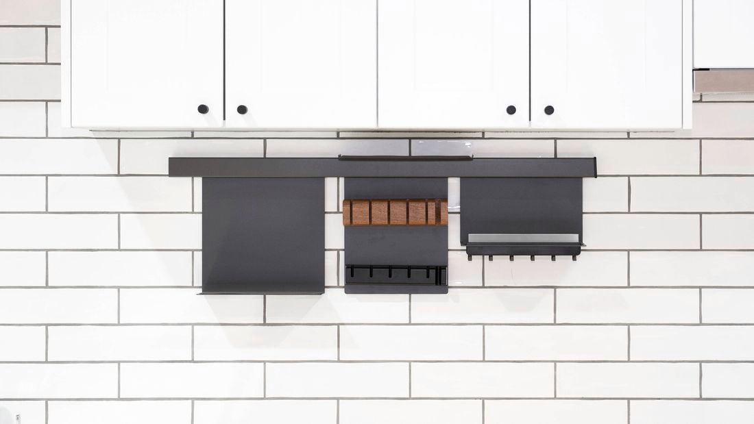 A wall with white tiles on it, white cupboards attached to it and black wall-mounted kitchen storage racks.