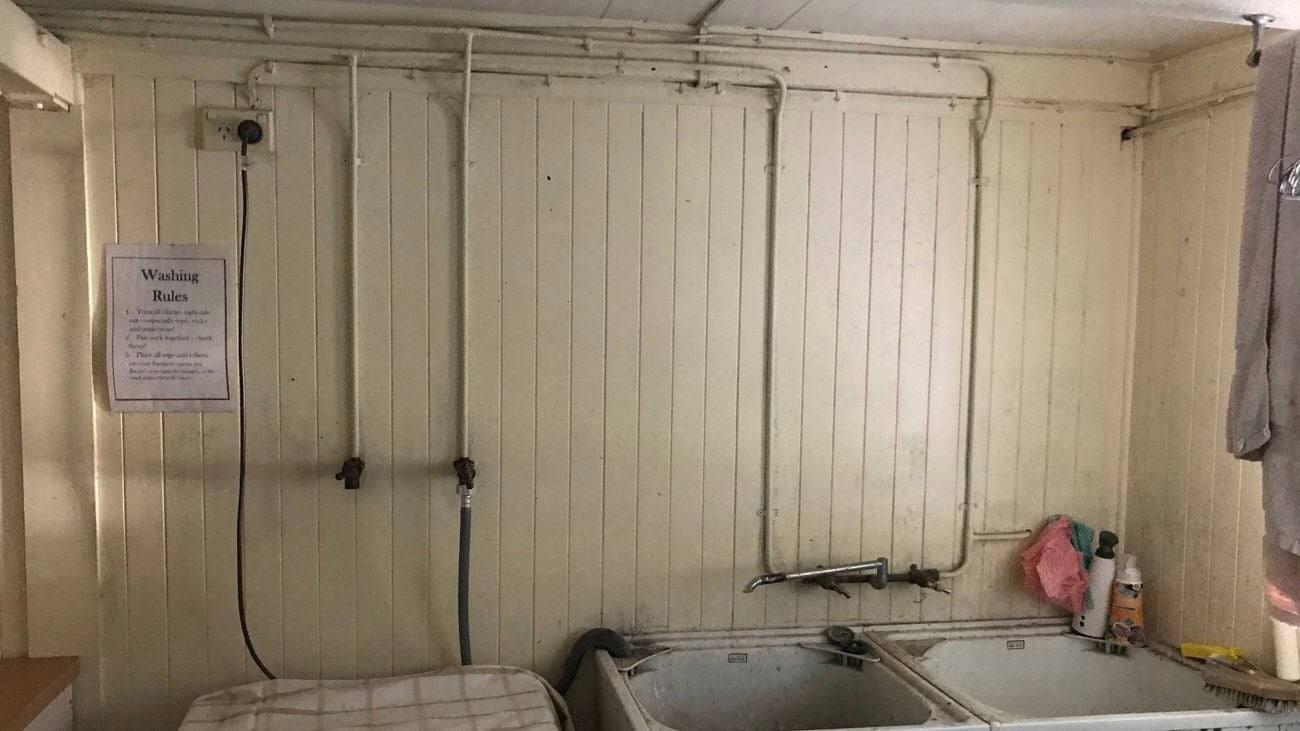 A room with pipes on the wall and sinks attached to the wall.