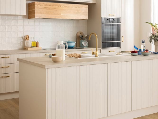 Beige modern kitchen on an angle, with brown benchtops that have crockery on it and an oven in it.