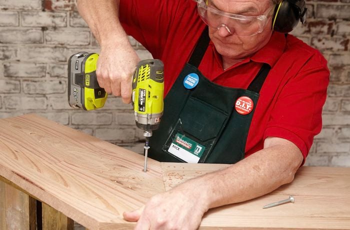 A Bunnings team member screwing a bar counter down onto a frame constructed from wooden pallets
