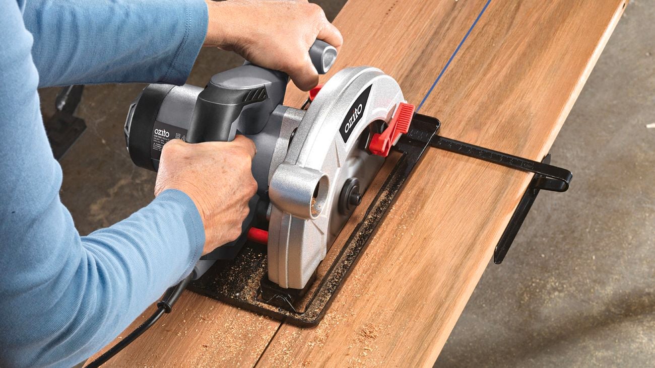 A person pushing an Ozito circular saw through a plank of wood to cut it in half