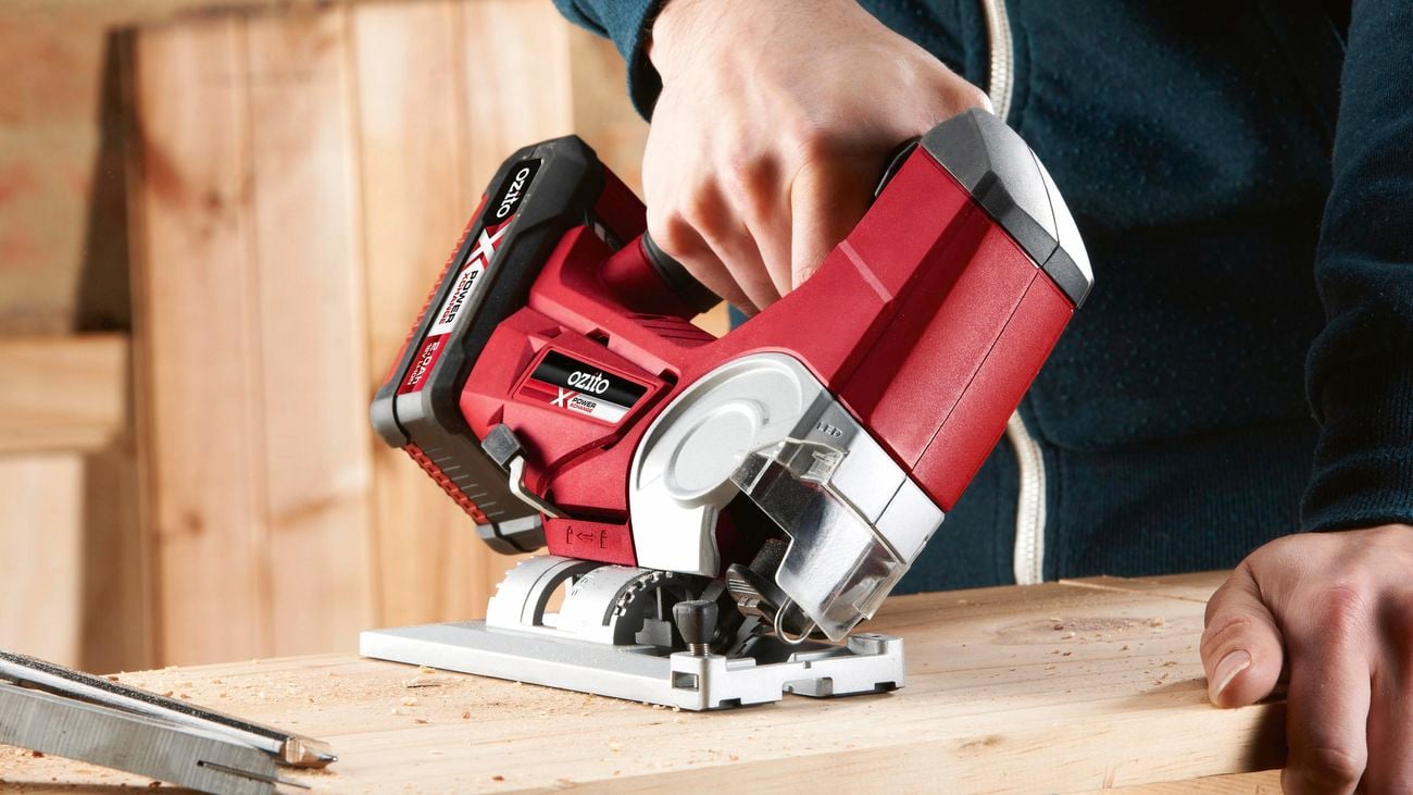 Person using a red, jigsaw power tool to cut through a plank of wood