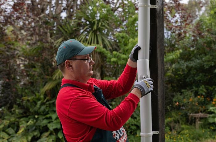 A Bunnings employee holding white, downpipe in his hands.