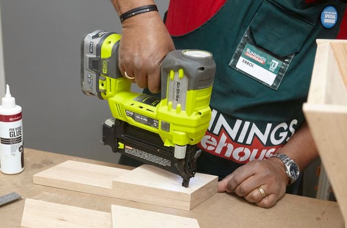 Person using nail gun to secure DIY wooden step stool support piece.
