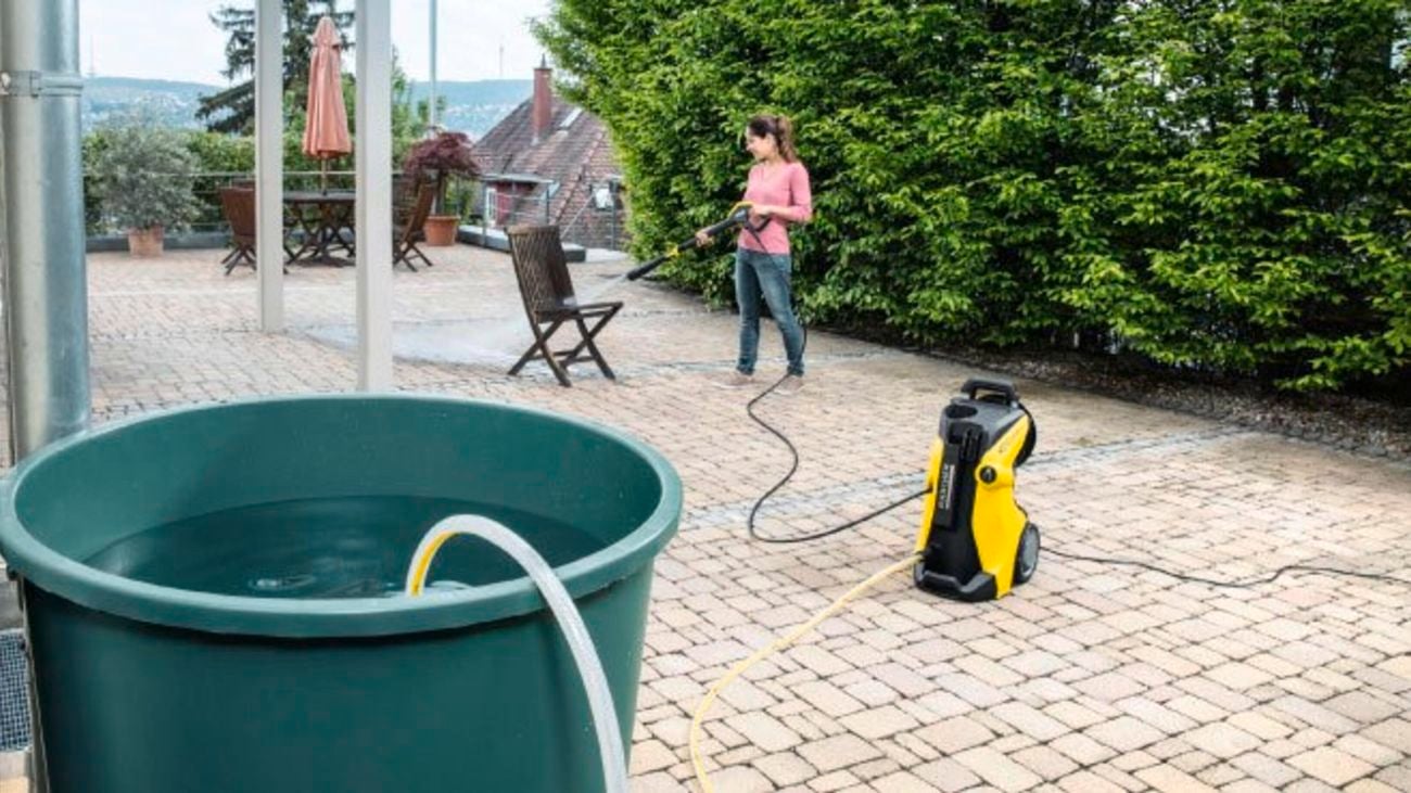 A woman using a pressure hose fed from a tub of grey water instead of a tap