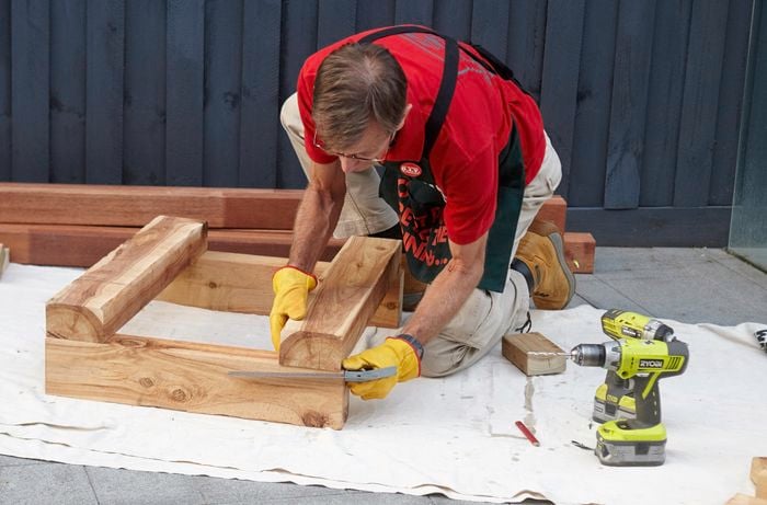 Framework for one end of a wooden outdoor day bed being measured for squareness with a square rule