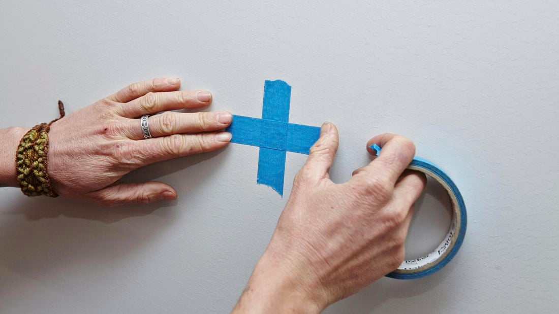 A person marking a wall with masking tape