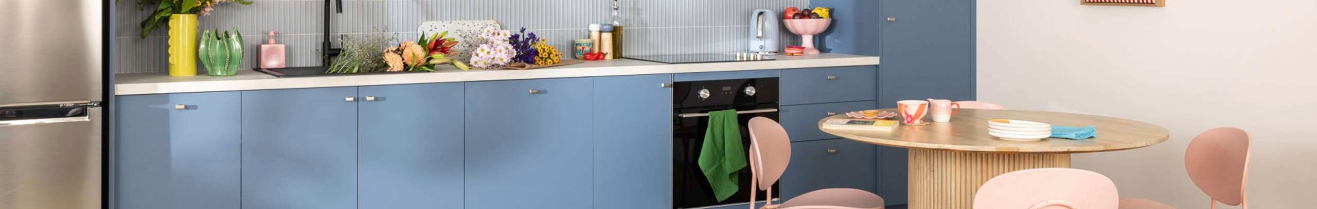 Blue modern kitchen, with items on the benchtop, a fridge and table and chairs in it.
