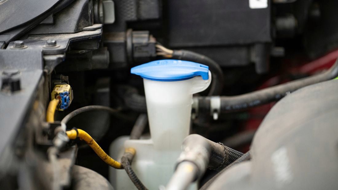 A car’s windshield washer fluid reservoir is shown with its blue cap closed.